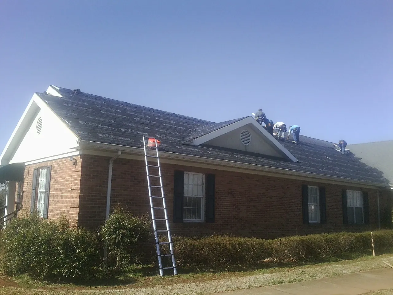 Crew tearing shingles off a brick ranch roof with a ladder set — Metal Roof Repair work by our crew in Atherton