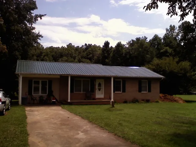 Dark green metal roof on a brick ranch with a covered porch in Atherton