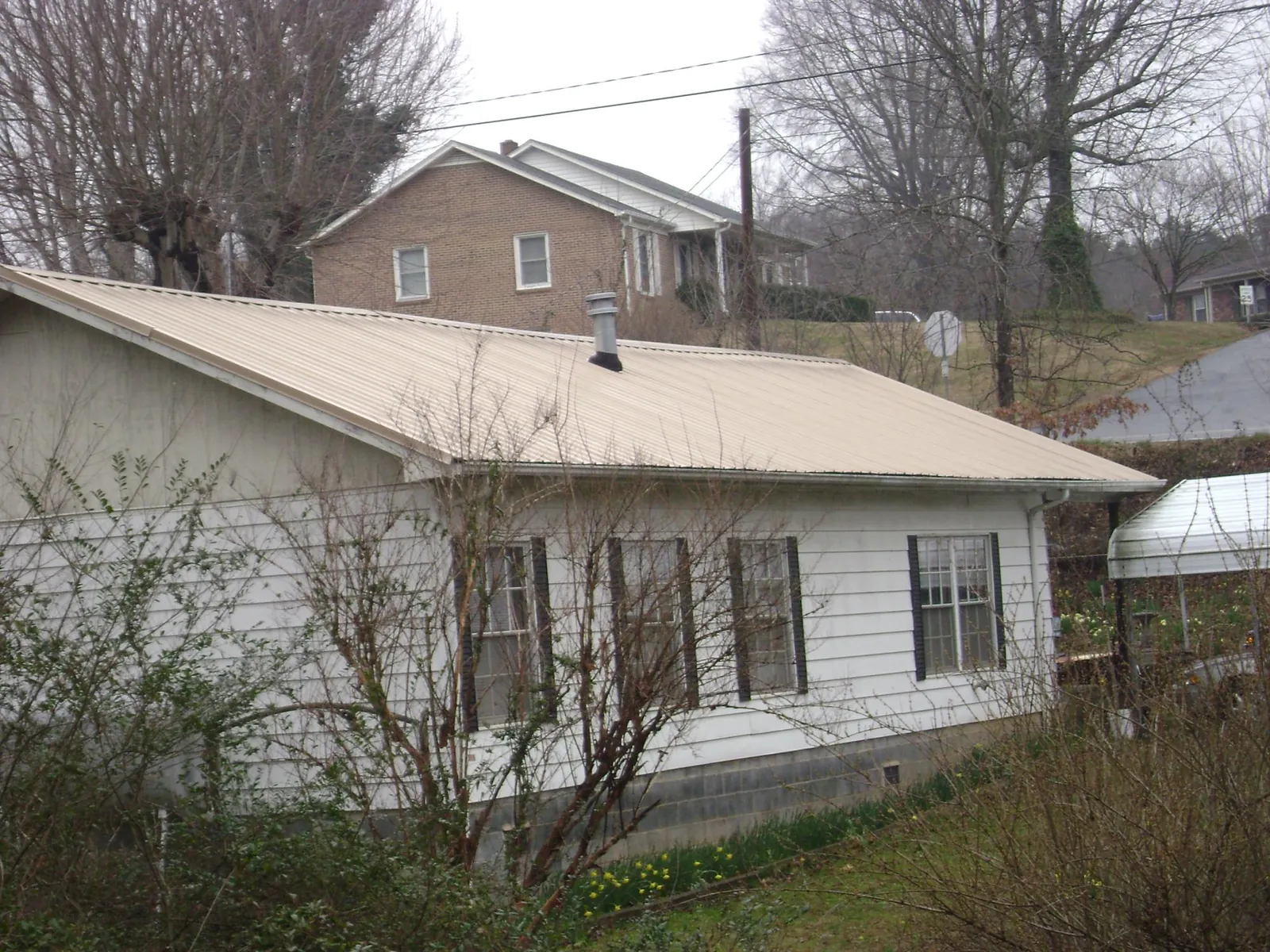 Tan metal roof on a white sided house set into a hillside — Commercial Roofing by Roofing Brothers in Atherton